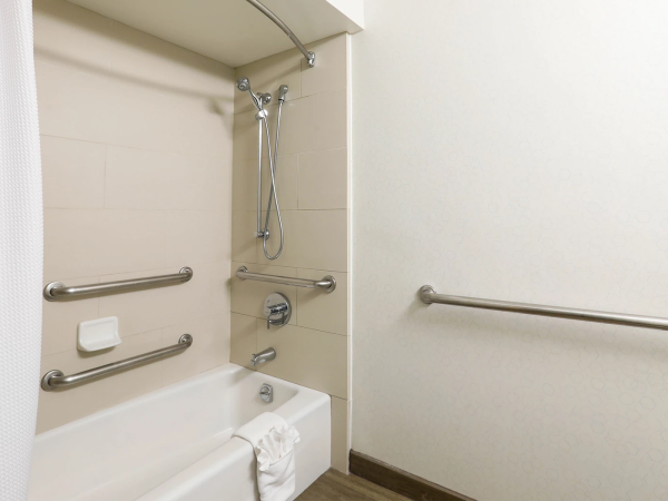 A accessible bathroom with a bathtub and shower, grab bars on walls, a handheld shower head, a shower curtain, and a towel on the tub edge.