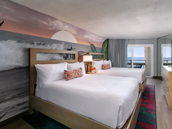 A hotel room with two queen beds, a sunset mural, sea view from the window, and modern decor, ending with a seaside vibe.