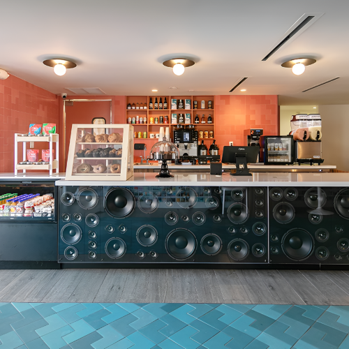 A bright bar area with a long dark counter, bottles on shelves, bar stools, and warm lighting.