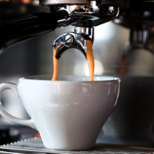 A coffee machine pouring rich espresso into a white cup, steam rising as the caramel-brown coffee fills the cup beneath the spout.