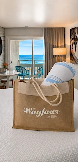 A beachside hotel room with a bag on the bed, sliding glass doors to a balcony, and ocean view in the distance.